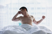 Man sitting in bed, stretching - Asia Images Group