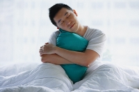Man sitting in bed, embracing pillow - Asia Images Group