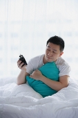 Man sitting in bed, holding alarm clock - Asia Images Group