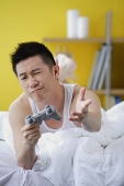 Man lying on bed, playing video game, making a face - Asia Images Group
