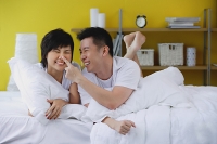 Couple lying on bed, man touching woman's nose - Asia Images Group