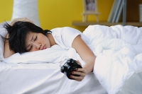 Woman in bed, looking at alarm clock, frowning - Asia Images Group