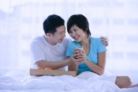 Couple sitting on bed, having breakfast, woman holding glass of milk - Asia Images Group