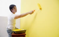 Man painting wall with yellow paint - Asia Images Group