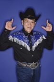 Senior man dressed in cowboy attire, making hand sign - Asia Images Group