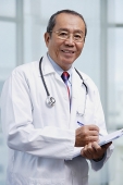 Doctor writing on medical chart, looking at camera - Asia Images Group