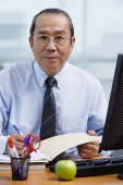 Businessman sitting at his desk, looking at camera - Asia Images Group