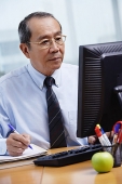 Businessman sitting at his desk, looking at computer - Asia Images Group
