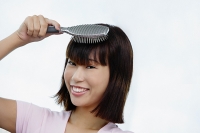 Young woman brushing her hair, smiling at camera - Asia Images Group