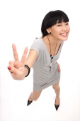 Young woman smiling up at camera, making peace sign - Asia Images Group