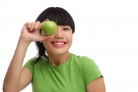 Young woman in green T-shirt holding green apple over eye - Asia Images Group