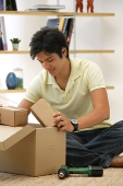 Man sitting on floor, looking through box - Asia Images Group