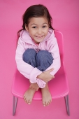 Girl sitting on chair, hugging knees, smiling up at camera - Asia Images Group