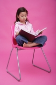 Girl on chair, reading a book, frowning - Asia Images Group