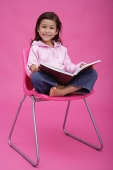 Girl on chair, reading a book, smiling at camera - Asia Images Group