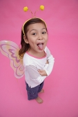 Young girl wearing fairy wings and deely bopper, arms crossed, sticking out tongue - Asia Images Group