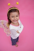 Young girl wearing fairy wings and deely bopper, arms crossed, smiling at camera - Asia Images Group
