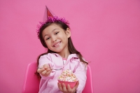 Girl wearing party hat, holding bowl of cake towards camera - Asia Images Group