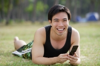 Man lying on grass, holding mobile phone - Asia Images Group