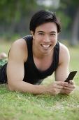 Man lying on grass, holding mobile phone, smiling at camera - Asia Images Group