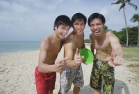 Men on beach, standing side by side, making hand sign - Asia Images Group