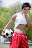 Young man with soccer ball, wiping chin with T shirt - Asia Images Group