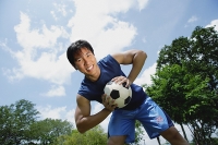 Man holding soccer ball, smiling at camera - Asia Images Group