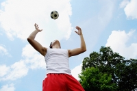 Man playing soccer, looking up at ball - Asia Images Group