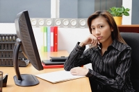 Female executive at desk, hand on chin - Asia Images Group