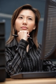 Female executive at desk, hand on chin, looking away - Asia Images Group