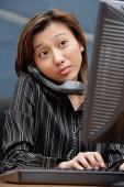Female executive at desk, using computer and telephone - Asia Images Group