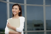 Female executive hugging folders, smiling, looking away - Asia Images Group