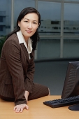 Businesswoman sitting on table, looking at camera - Asia Images Group