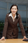 Businesswoman leaning on table, looking at camera - Asia Images Group