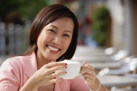 Woman in cafe holding coffee cup, smiling at camera - Asia Images Group