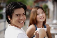 Couple in cafe having coffee, focus on man in foreground, smiling at camera - Asia Images Group