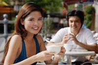 Woman sitting in cafe, having coffee, man in the background - Asia Images Group