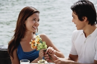 Couple sitting at outdoor cafe, man handing a woman flowers - Asia Images Group