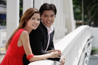 Couple leaning over bridge railing, looking at camera - Asia Images Group