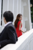 Man leaning on bridge railing, woman in background turning to look at him - Asia Images Group