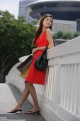 Woman with shopping bags, leaning on railing, looking away - Asia Images Group
