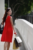 Woman in red dress carrying shopping bags, looking over shoulder - Asia Images Group