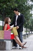 Woman sitting on park bench, looking at man standing next to her - Asia Images Group