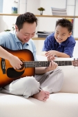 Father playing the guitar, son watching him - Asia Images Group