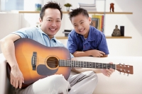 Father and son smiling at camera, father holding guitar - Asia Images Group