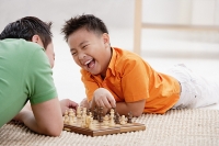 Father and son lying on floor, playing chess, laughing - Asia Images Group