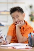 Boy doing homework, smiling at camera, hand on chin - Asia Images Group