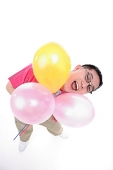 Man holding  three balloons, looking up at camera, mouth open - Asia Images Group