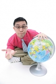 Man sitting on floor, hand on globe, shrugging - Asia Images Group