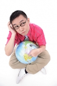 Man sitting on floor, holding globe, thinking - Asia Images Group